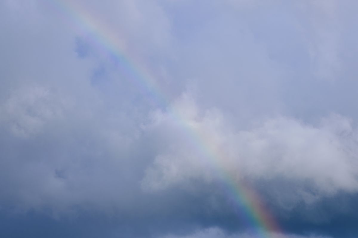 A rainbow arcing across a cloudy sky, dispersion of sunlight in raindrops