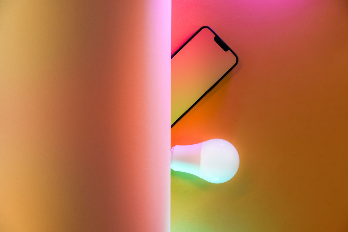 A smart light bulb glowing in colour beside a smartphone