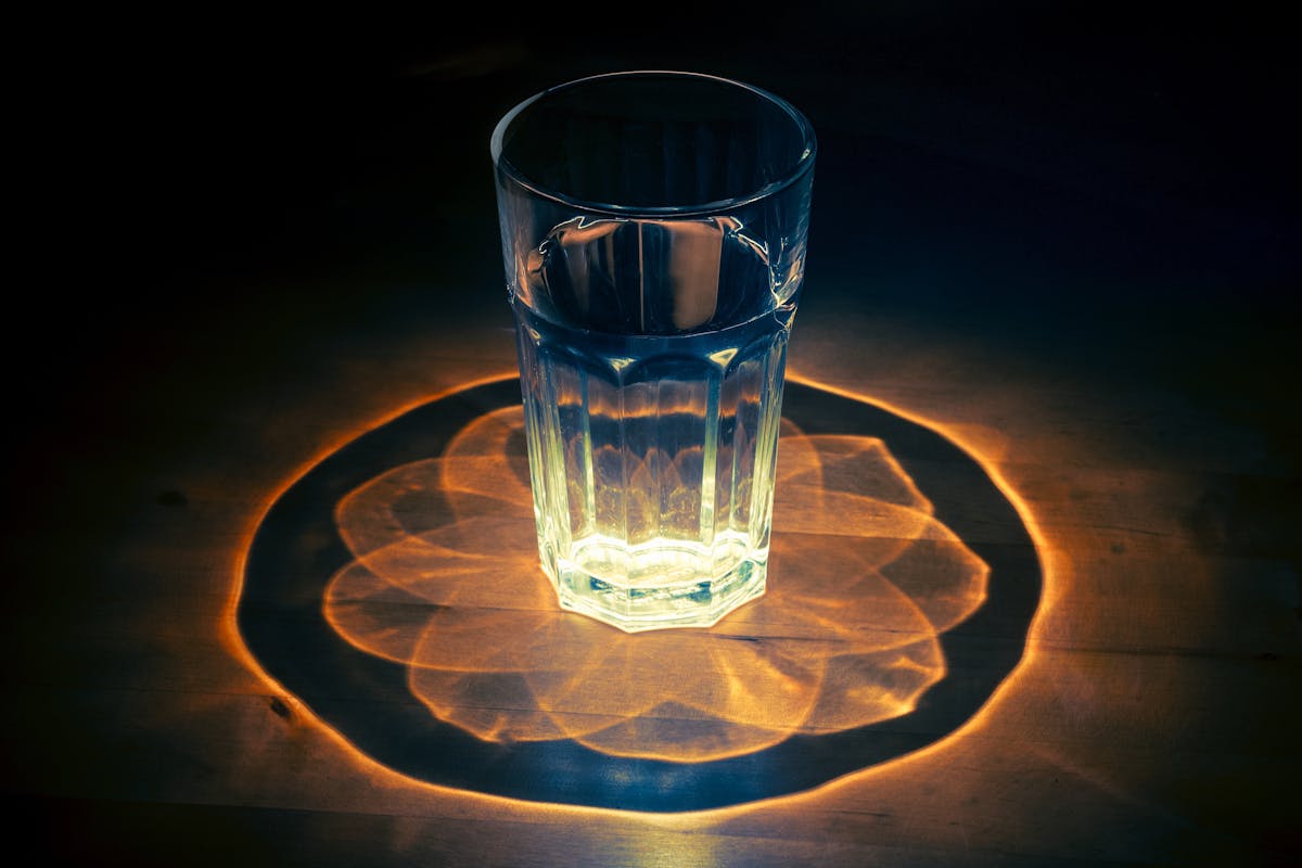 A glass of water bending light and casting bright patterns on a table
