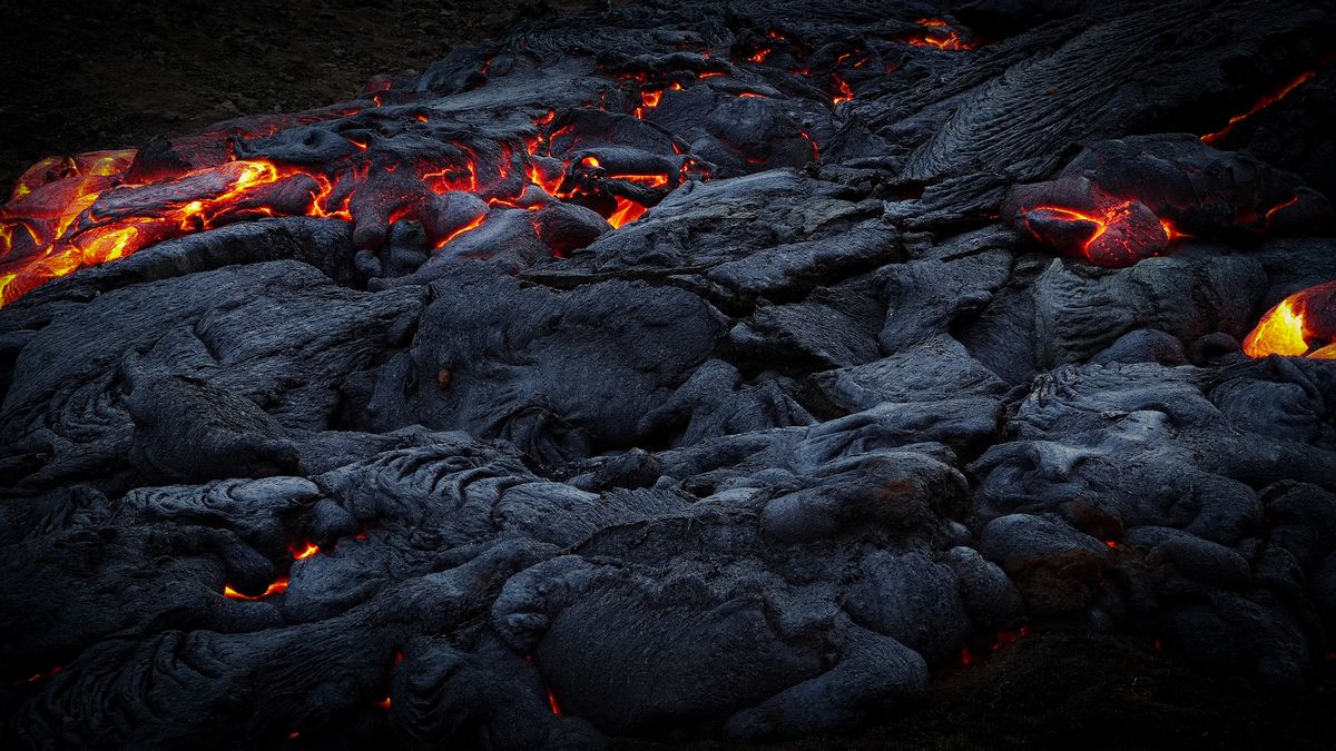 Glowing molten lava flowing over dark rock, natural light from heat