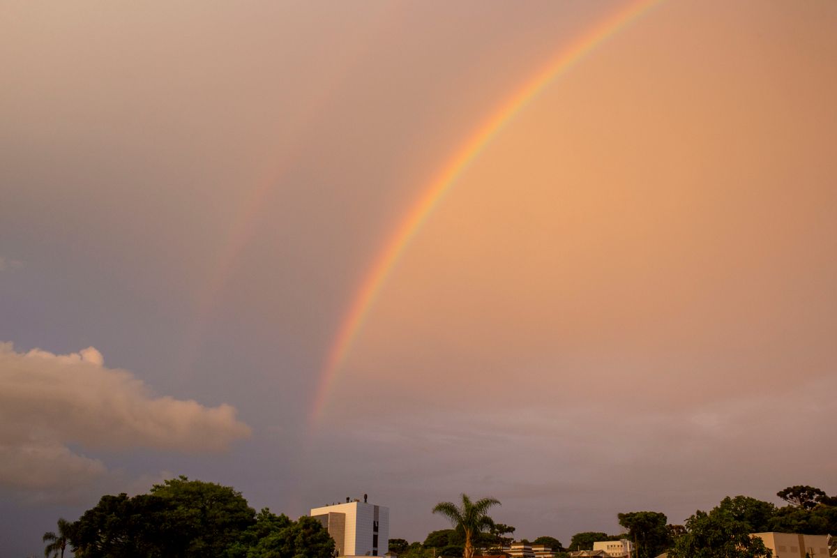 a breathtaking double rainbow arcs across a serene blue sky creating a vibrant natural spectacle