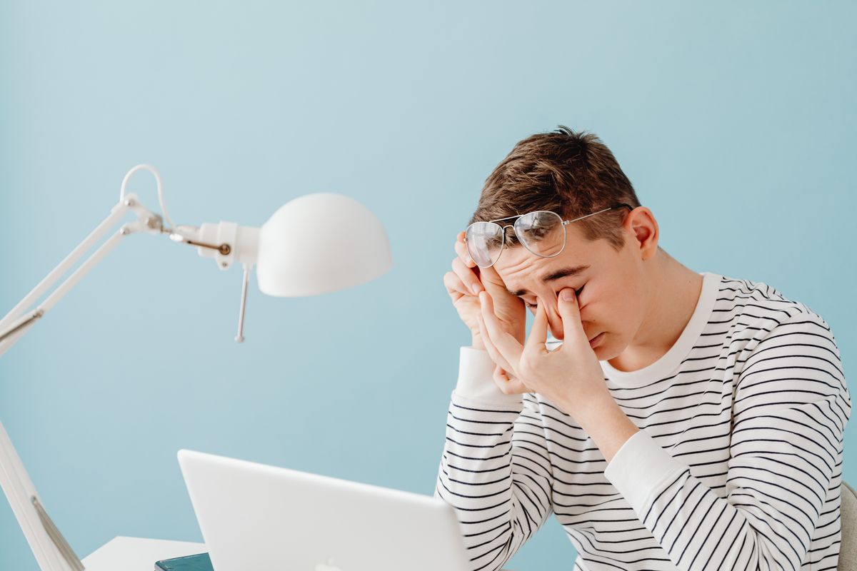 A tired man rubbing his eyes at a laptop, the eye strain blue light glasses claim to fix